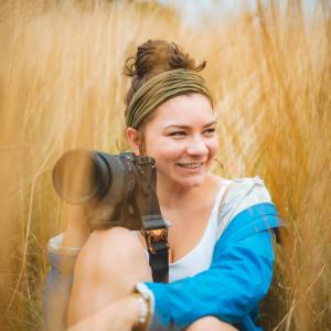 Holly Fasching sitting in a field holding her camera. 