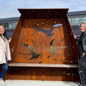 Katie Bui ’26 and Deirdre Murphy celebrate World Migratory Bird Day at Washington College in Maryland, standing by their public art commission, Flyways.