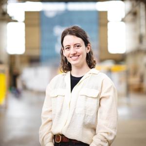 Lauren Scott stands in high bay C for a portrait wearing a tan button up shirt.