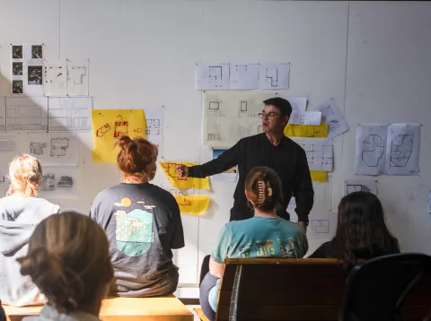Art, architecture and design students facing a professor presenting his work.