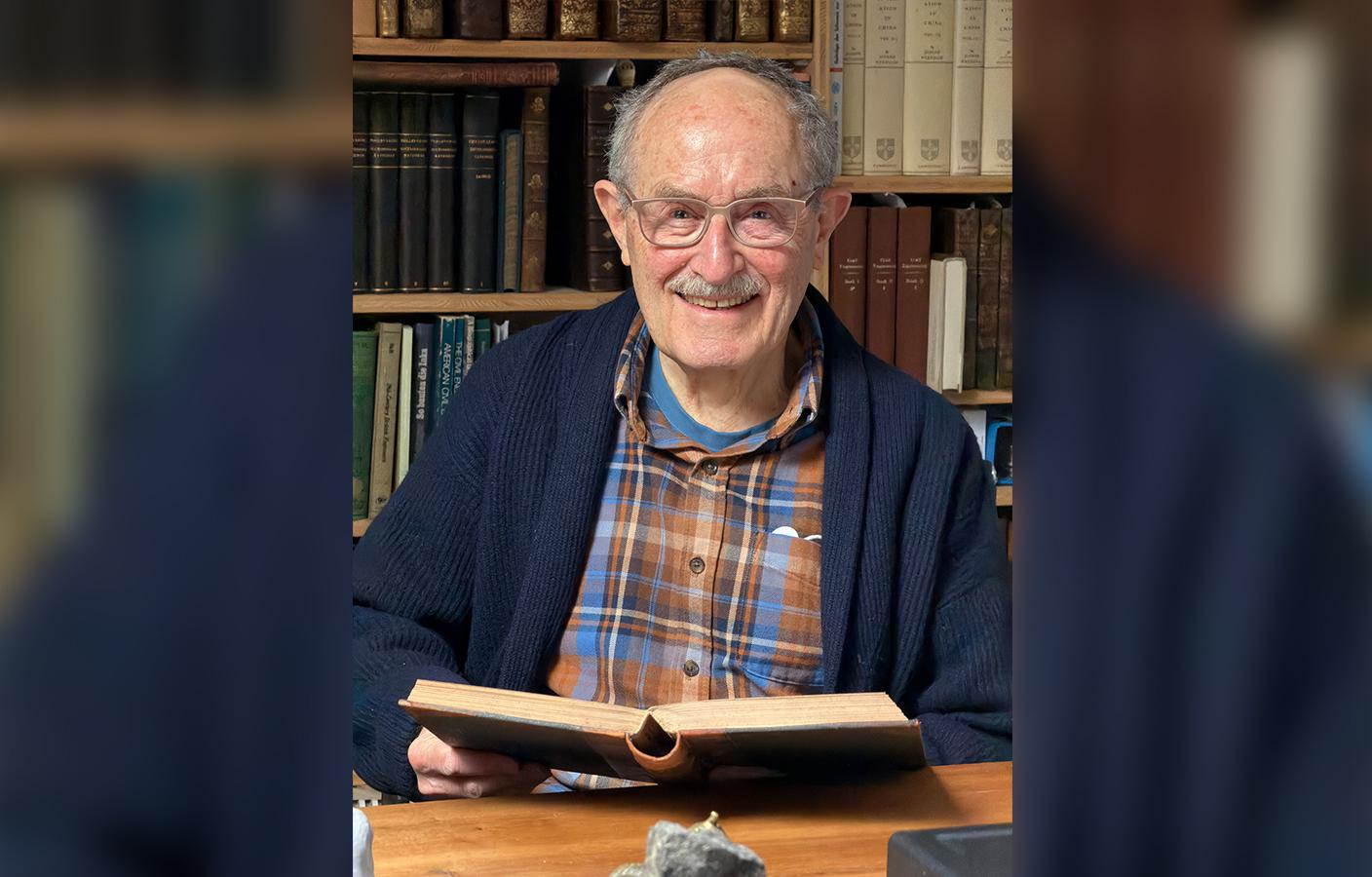 Tom Peters in his office smiling while holding an open book.