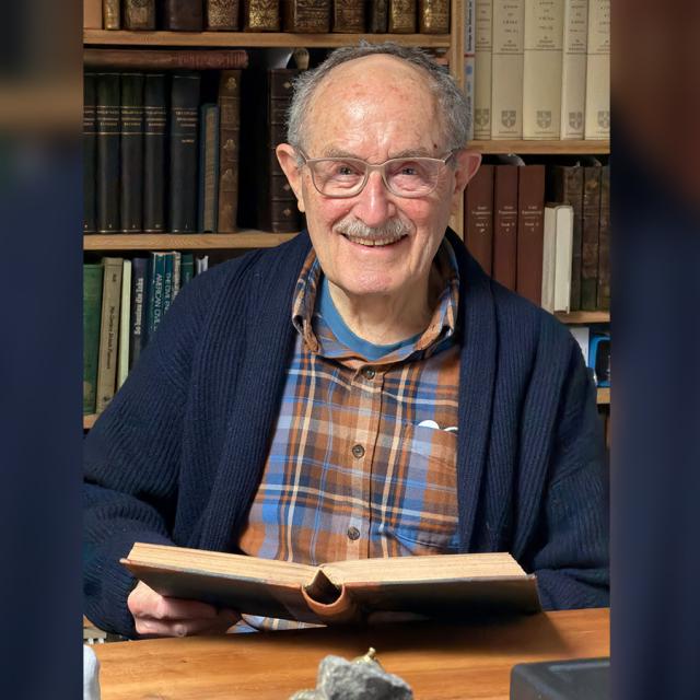 Tom Peters in his office smiling while holding an open book.
