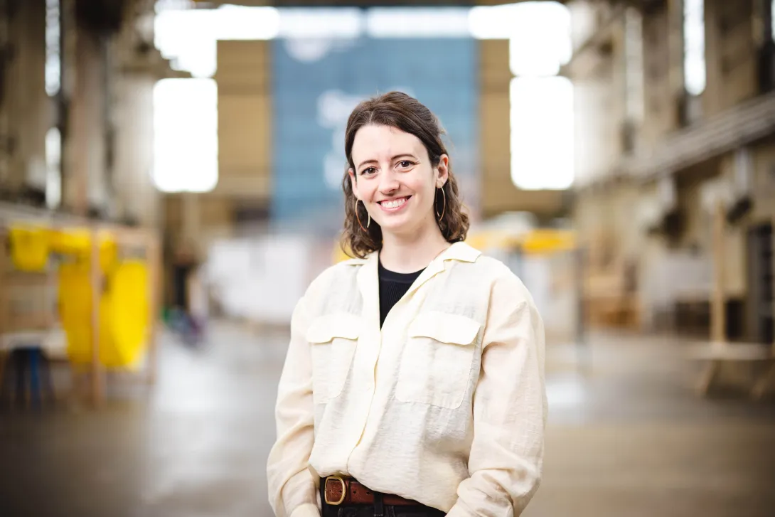 Lauren Scott stands in high bay C for a portrait wearing a tan button up shirt.