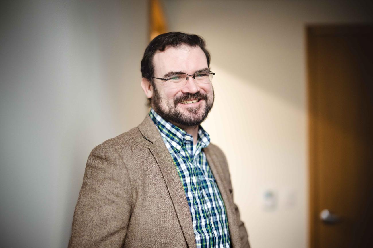 Patrick Cox smiles for a portrait in a hallway.